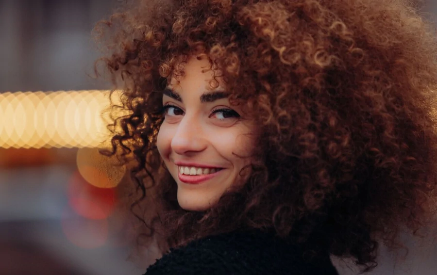 Primo piano di una donna con capelli ricci definiti e lucenti, curati con la giusta routine quotidiana